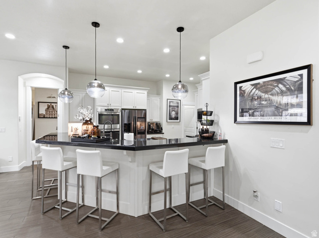 1154 Sunset Dunes Way Draper, UT 84020 - Photo 19 of 50 Kitchen featuring a breakfast bar area, a peninsula, hanging light fixtures, white cabinets, and stainless steel appliances