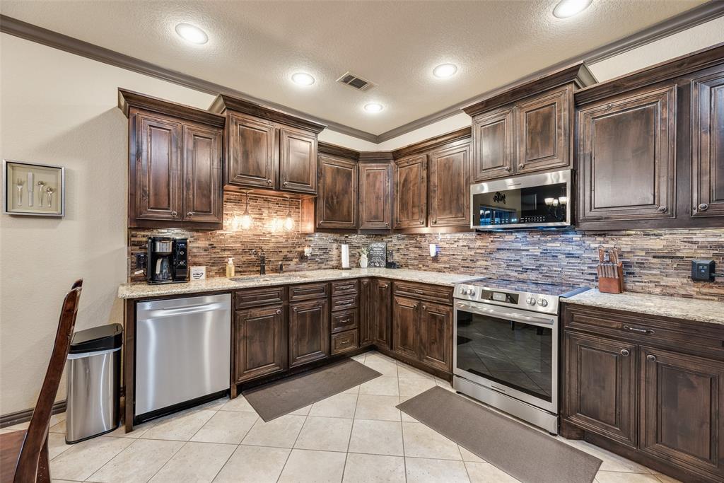 1132 Chartres Street Kaufman, TX 75142 - Photo 7 of 25 Kitchen featuring extensive dark wood cabinetry, light-toned countertops, and a full suite of stainless steel appliances