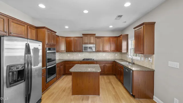 a kitchen with stainless steel appliances granite countertop a refrigerator a sink dishwasher a stove and a dining table with wooden floor