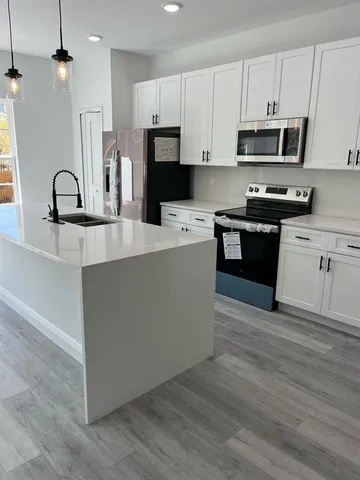 a kitchen with stainless steel appliances granite countertop a stove top oven a sink a refrigerator white cabinets and wooden floor