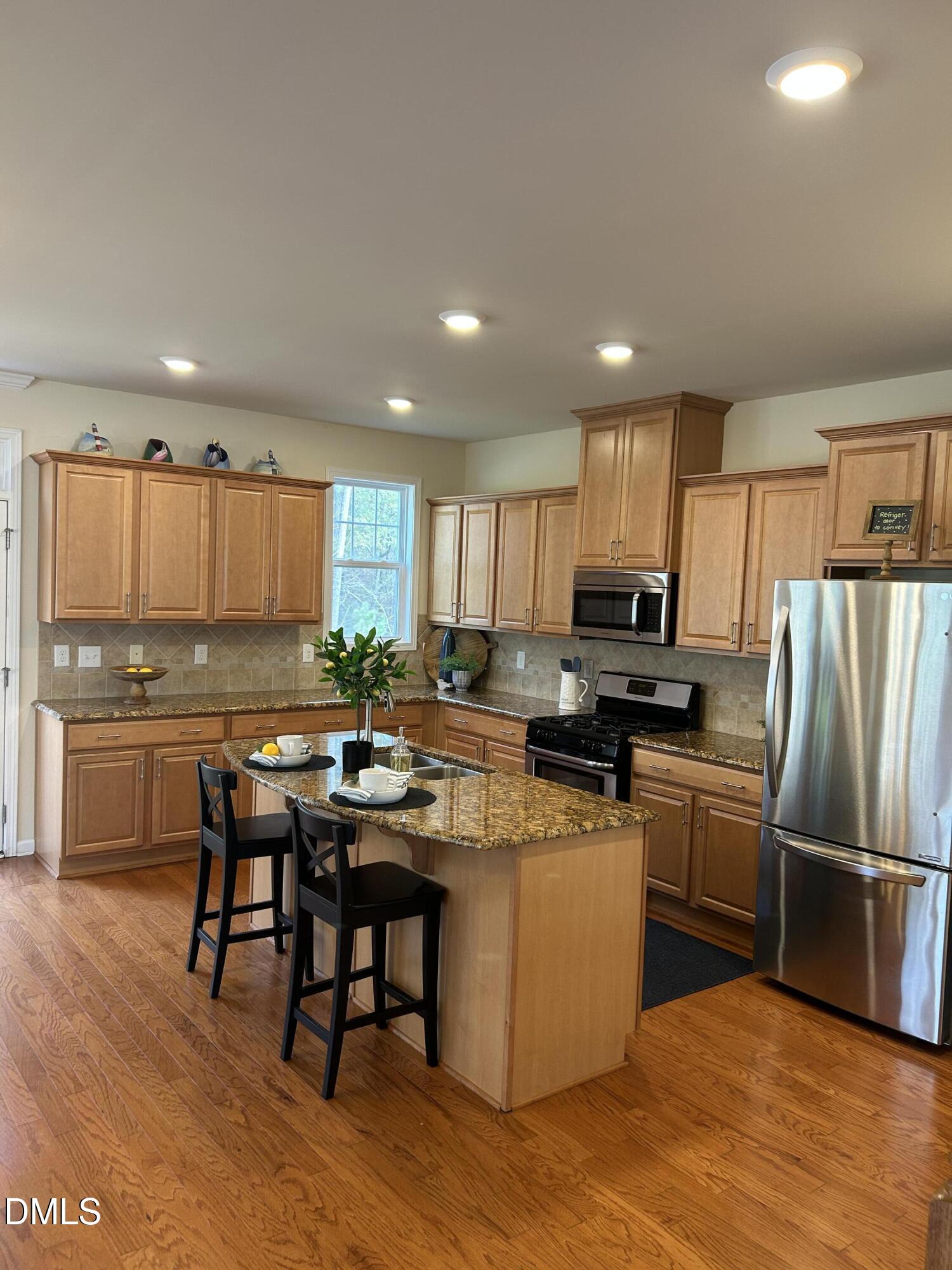 634 Edgewater Ridge Court Apex, NC 27523 - Photo 6 of 23 a kitchen with kitchen island granite countertop wooden floors and stainless steel appliances