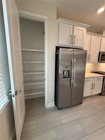 a view of a refrigerator in kitchen and an empty room with wooden floor