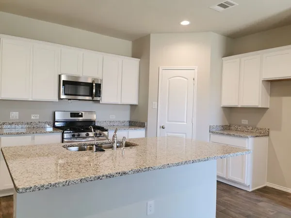 a kitchen with granite countertop a sink a stove a microwave a refrigerator and cabinets