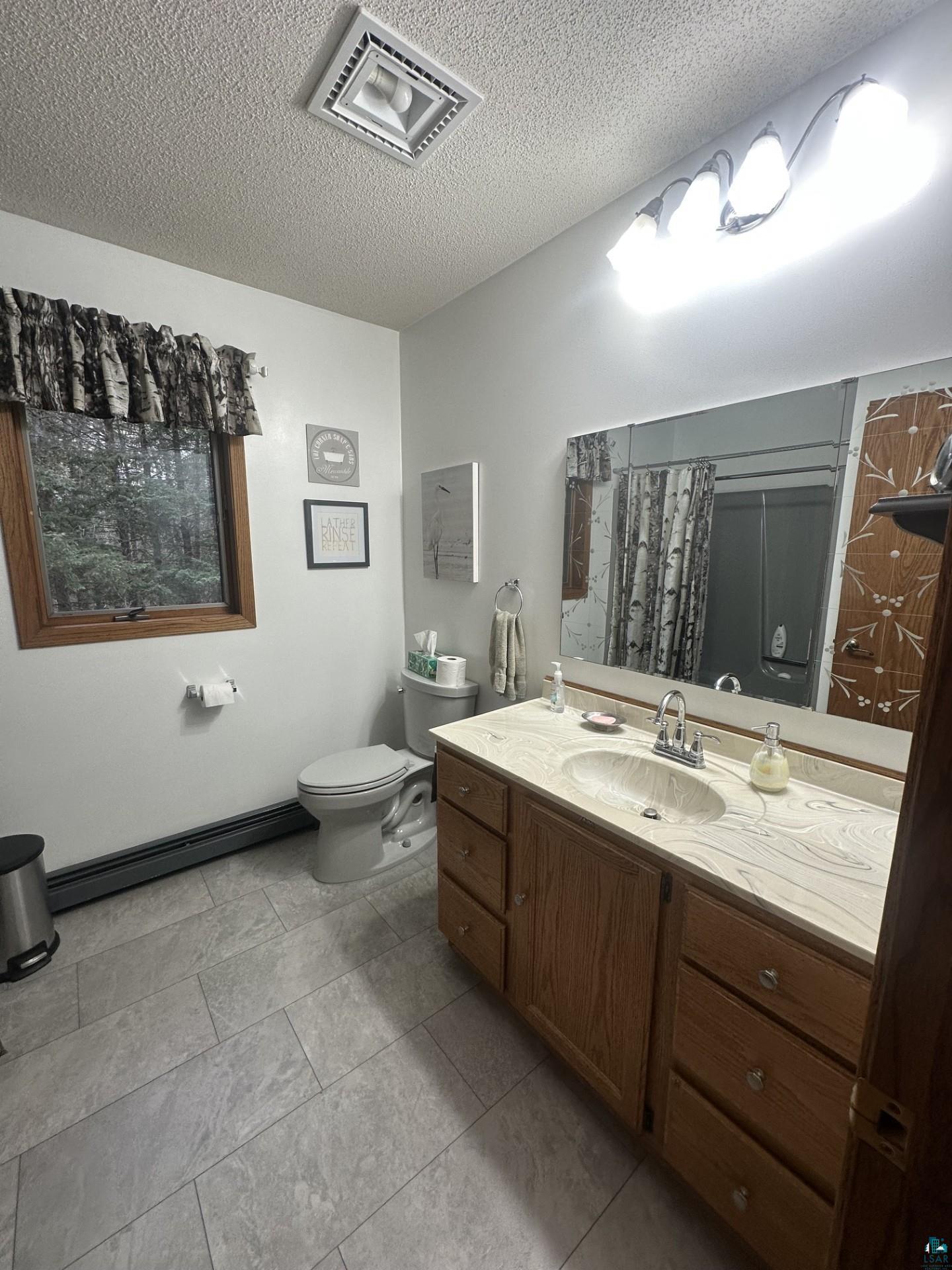 81 Hautaluoma Road Esko, MN 55733 - Photo 33 of 43 Bathroom featuring a wood vanity with a light-colored countertop and integrated sink, a rectangular mirror, a window with wood trim, and light gray rectangular floor tiles