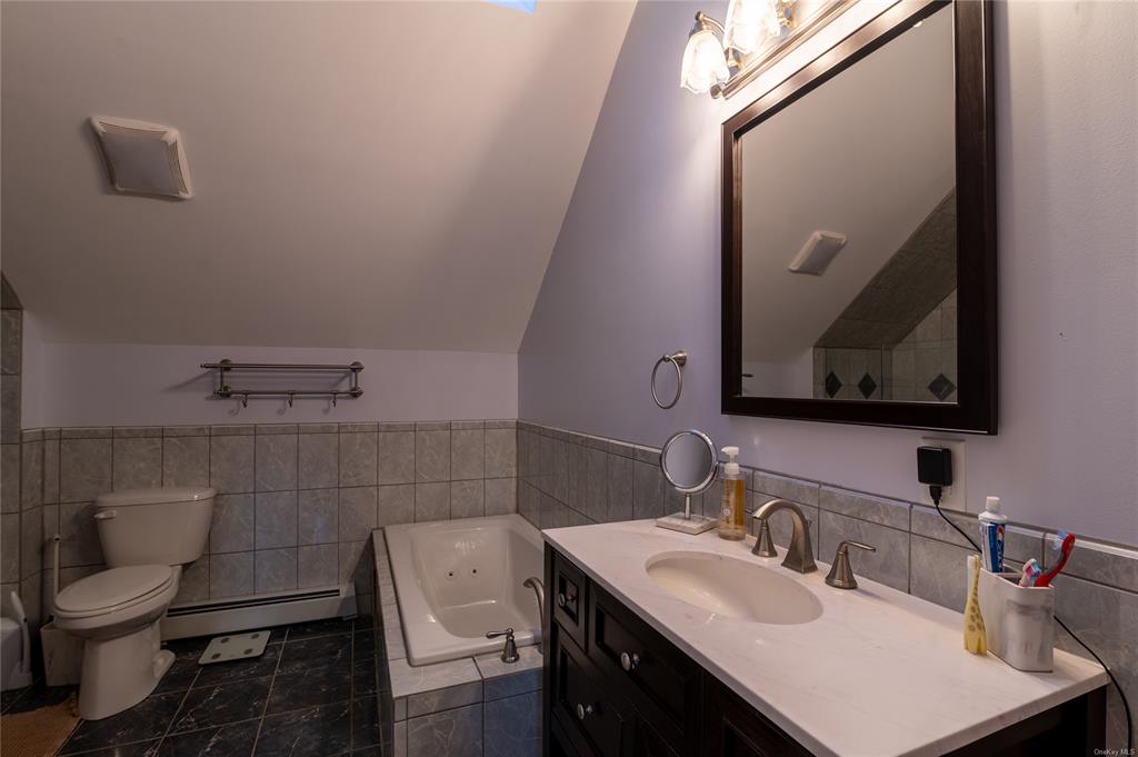 374 Hill Road Jeffersonville, NY 12748 - Photo 19 of 36 Bathroom with vanity, baseboard heating, a relaxing tiled tub, tile patterned flooring, and lofted ceiling