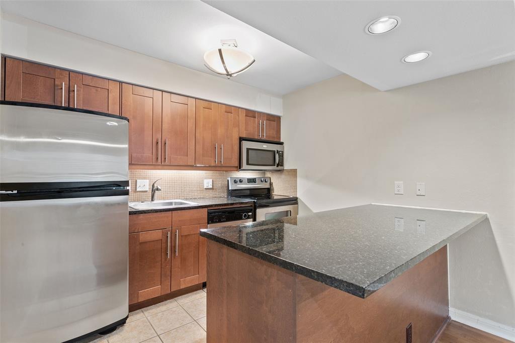 7685 Northcross Drive, Unit 423 Austin, TX 78757 - Photo 9 of 20 a kitchen with granite countertop a refrigerator a stove a sink and white cabinets