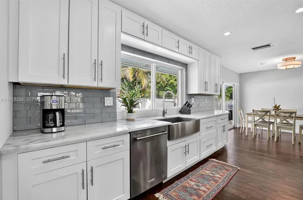 a kitchen with stainless steel appliances granite countertop a stove a sink and white cabinets with wooden floor