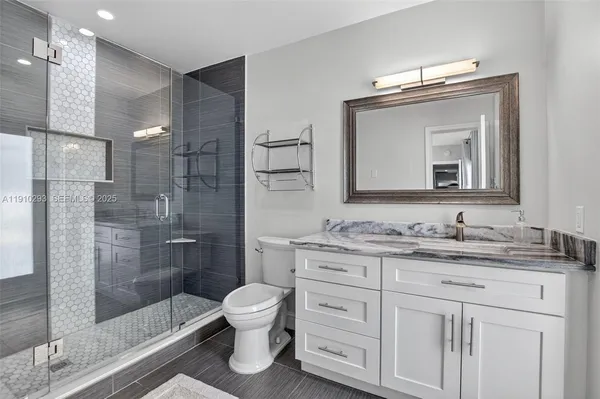 a bathroom with a toilet a sink a glass door a shower a mirror and vanity