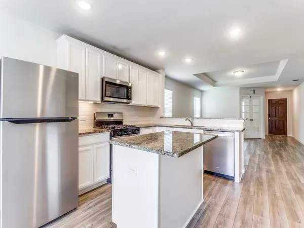 a kitchen with stainless steel appliances granite countertop a refrigerator a stove a sink dishwasher and a refrigerator with wooden floor