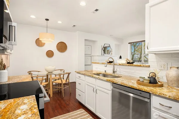a kitchen with stainless steel appliances granite countertop a sink a stove and a dining table with wooden floor