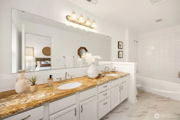 a bathroom with double vanity sinks a granite tub and mirror