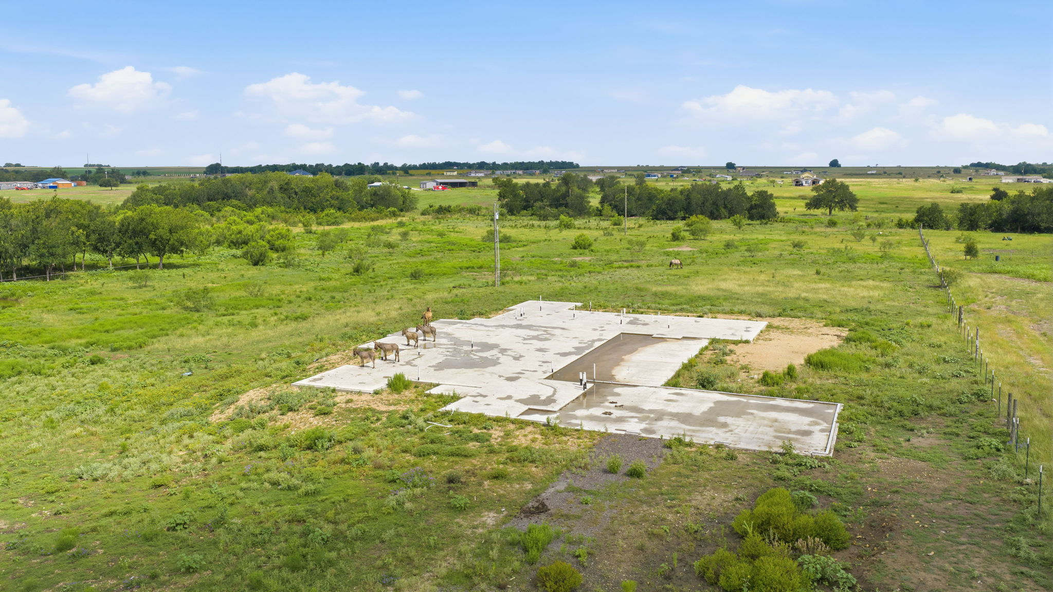 1701 County Road 466 Elgin, TX 78621 - Photo 13 of 24 A ready-to-build concrete foundation awaits amidst a sprawling green landscape, promising a spacious rural home.