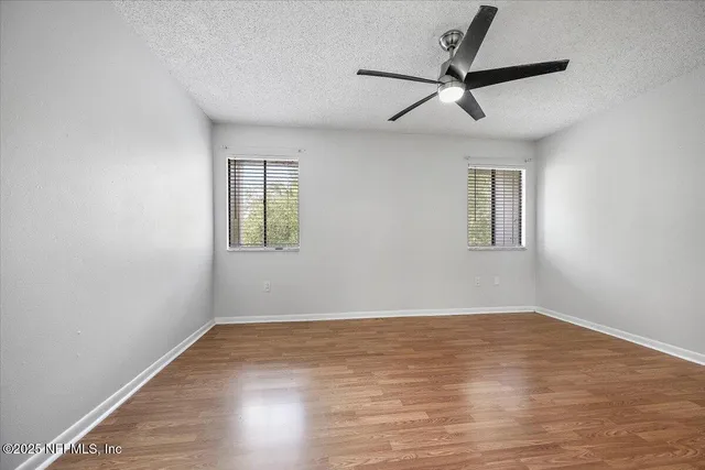 an empty room with wooden floor ceiling fan and windows