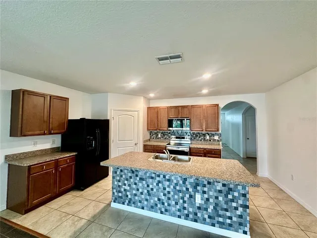 a kitchen with stainless steel appliances kitchen island granite countertop a refrigerator a stove a sink dishwasher and a oven with wooden cabinets