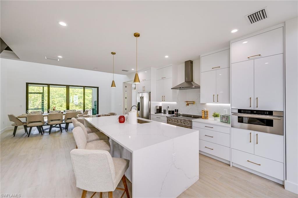 3400 Canal Street Naples, FL 34112 - Photo 7 of 34 a large kitchen with kitchen island a stove a sink a dining table and chairs with wooden floor