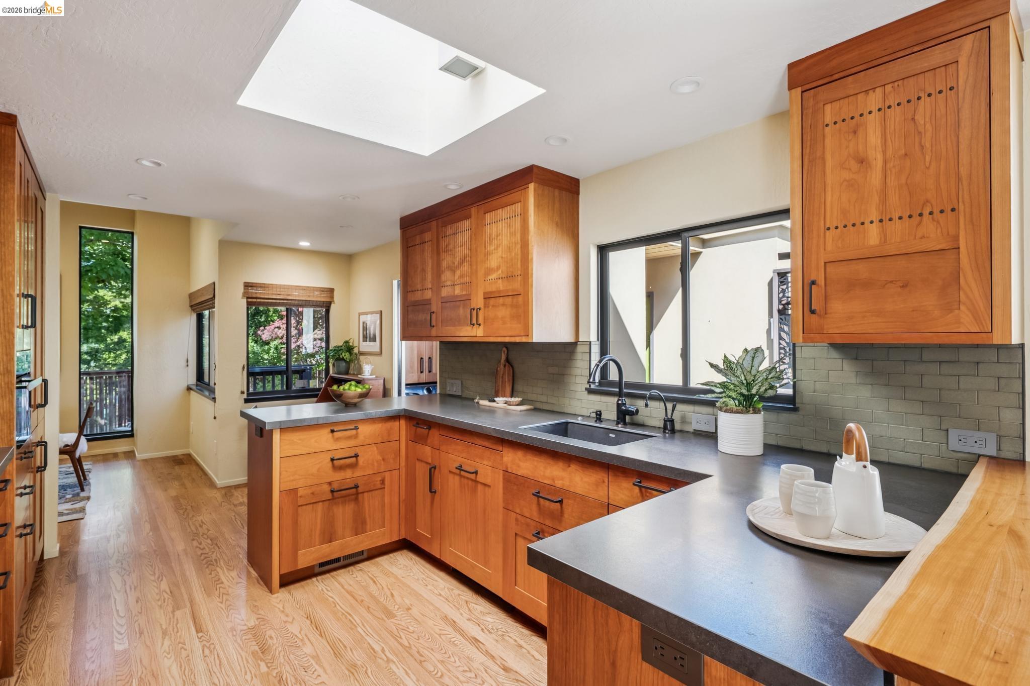 576 Vistamont Avenue Berkeley, CA 94708 - Photo 12 of 33 Kitchen featuring rich wood cabinetry, dark countertops, a recessed sink with a matte black faucet, a skylight, and wood-finish flooring