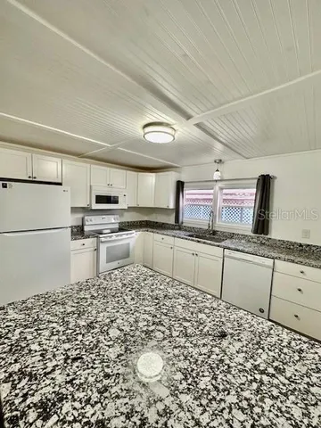 a kitchen with granite countertop a refrigerator and white cabinets