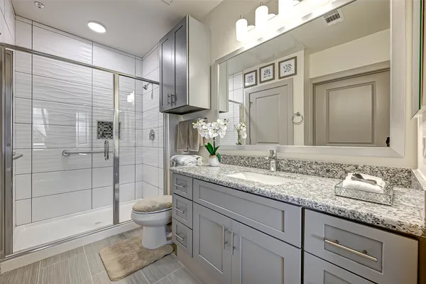 a bathroom with a granite countertop sink a toilet a mirror and shower
