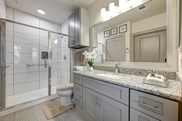 a bathroom with a granite countertop sink a toilet a mirror and shower