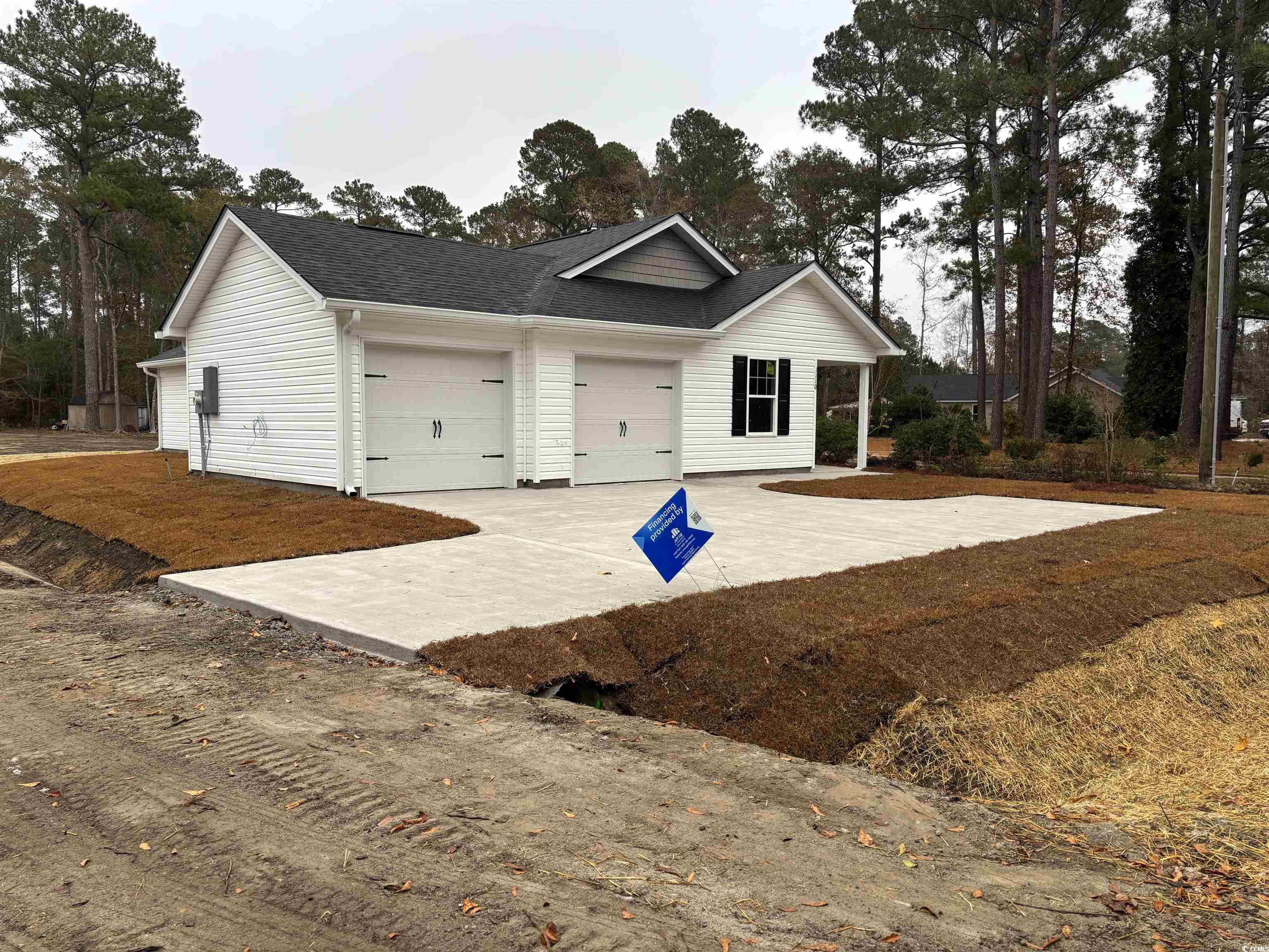 Ranch-style house with a shingled roof, concrete driveway, a garage, and view of scattered trees