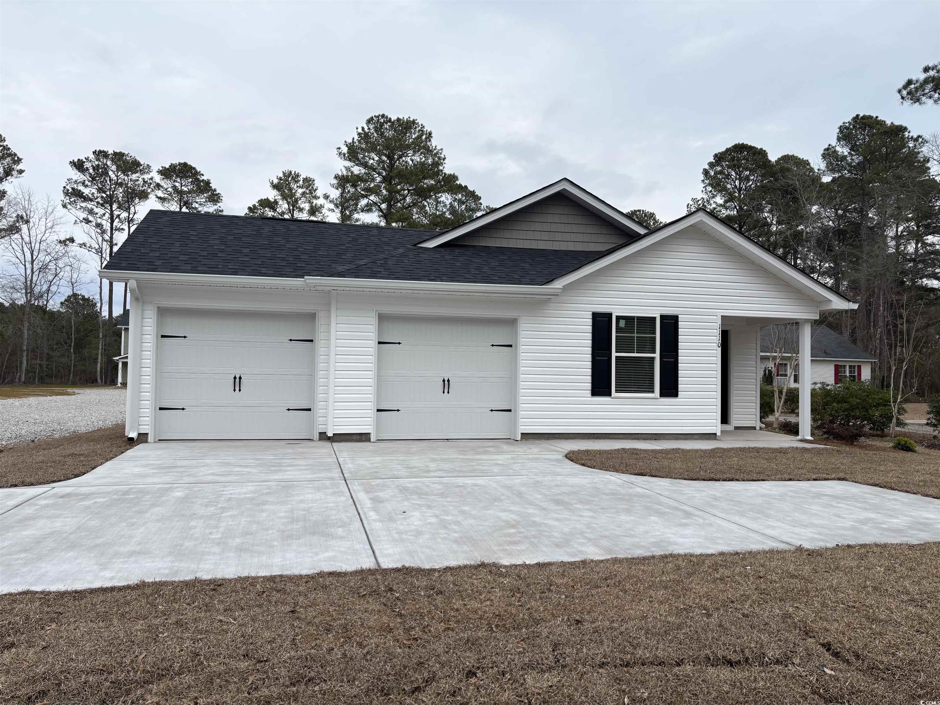 Ranch-style house with a shingled roof, concrete driveway, a garage, and view of scattered trees