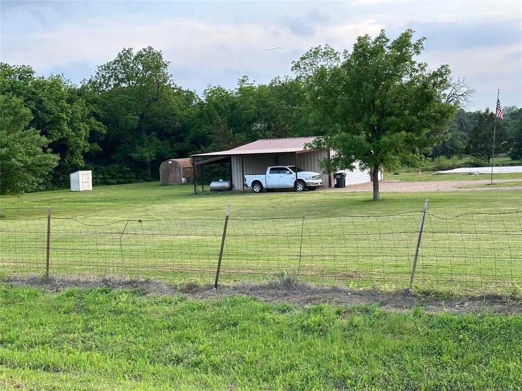 114 Earl Road Sadler, TX 76264 - Photo 16 of 16 Expansive green space with mature trees, a metal-roofed carport, and a storage shed