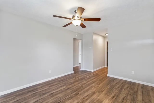a view of an empty room with wooden floor and a ceiling fan