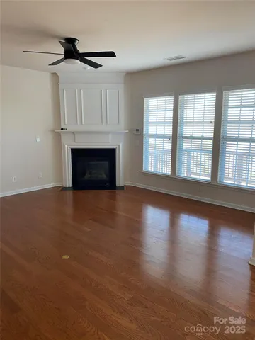 a view of an empty room with wooden floor fireplace and a window