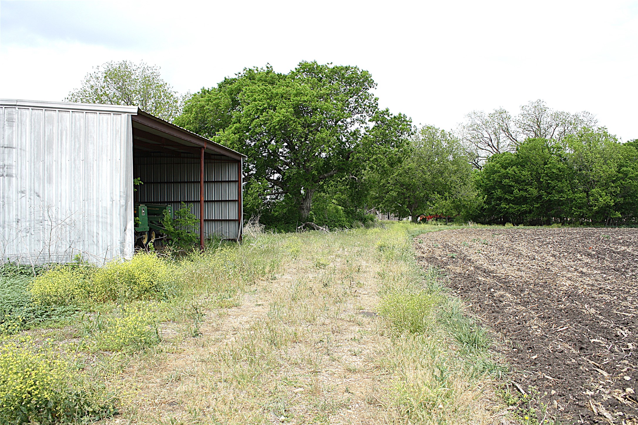 19374 Pennington Branch Road Holland, TX 76534 - Photo 14 of 24 The property includes a large metal-sided outbuilding, a cleared dirt path, and an expansive field of tilled soil