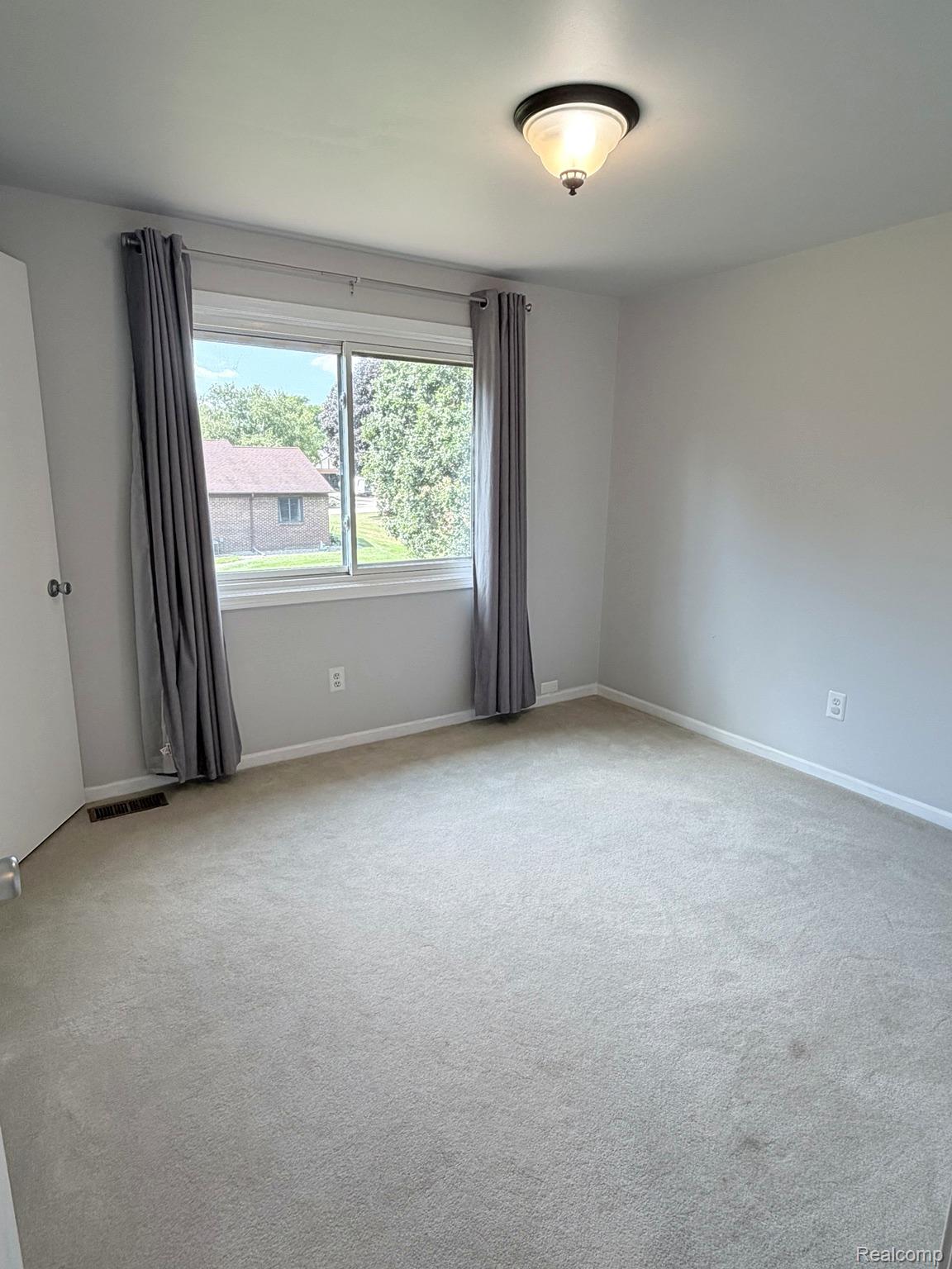 2070 Winchester Road Rochester, MI 48307 - Photo 24 of 34 Bright and spacious bedroom featuring neutral carpeting, large dual-pane windows with blackout curtains, ceiling-mounted light fixture, and fresh white walls with electrical outlets