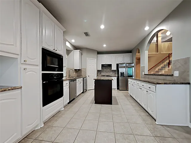 a large kitchen with stainless steel appliances granite countertop a stove top oven a sink dishwasher and a refrigerator