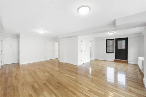 a view of an empty room with wooden floor and window