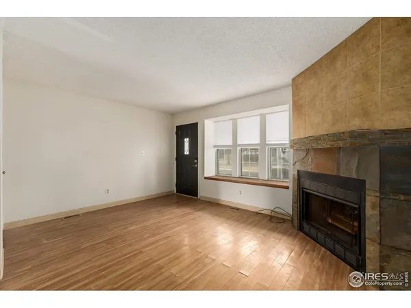a view of an empty room with wooden floor fireplace and a window