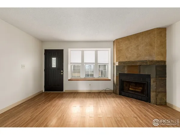 a view of an empty room with wooden floor fireplace and a window