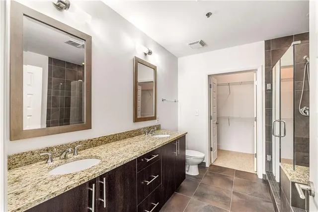 a bathroom with a granite countertop sink a toilet a mirror and shower