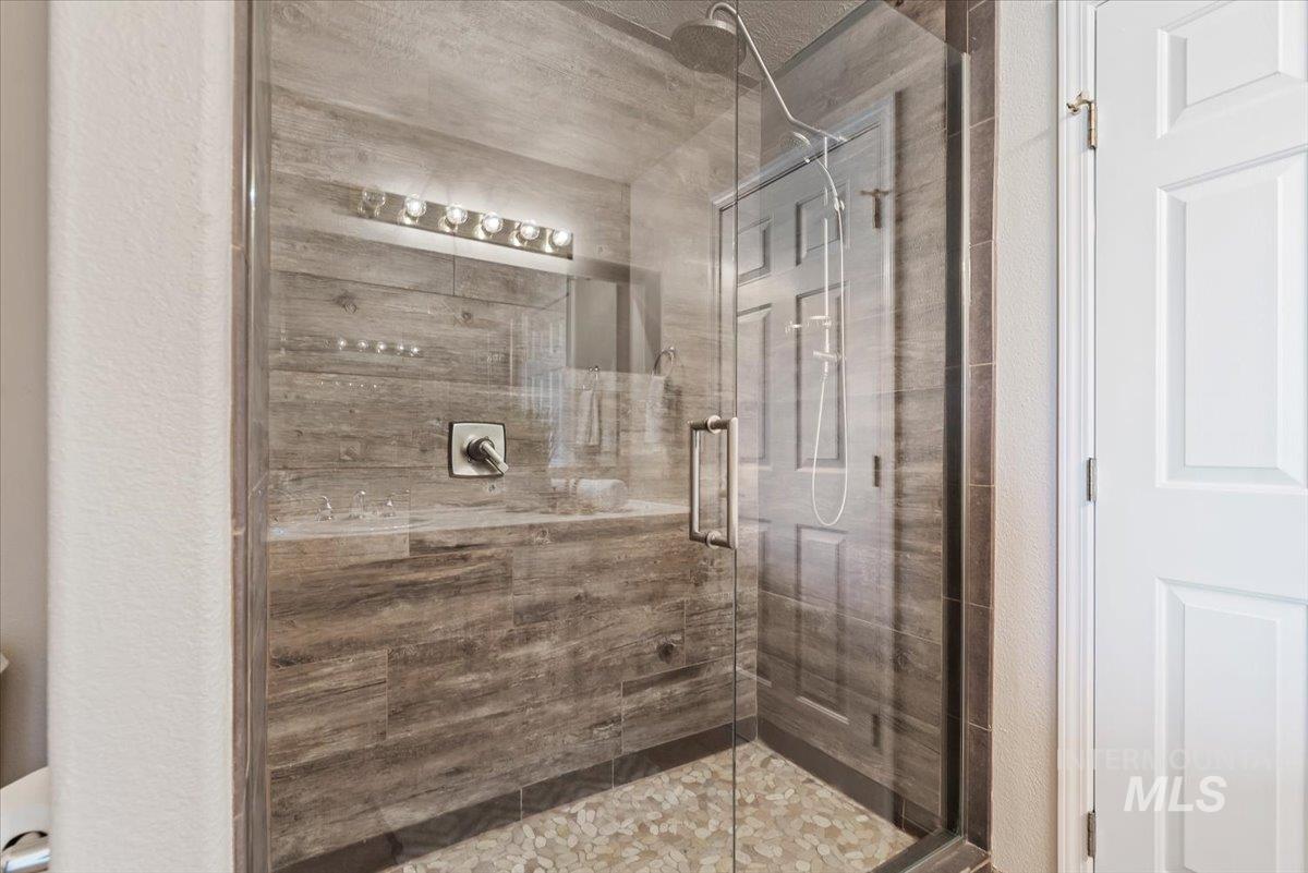 147 East Indian Crk Road Boise, ID 83716 - Photo 21 of 43 Glass-enclosed shower with wood-finish tile walls, pebble flooring, and a chrome rain shower head