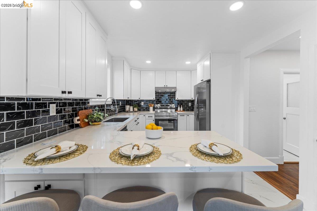 2717 Mabel Street Berkeley, CA 94702 - Photo 37 of 60 Kitchen with light stone counters, white cabinetry, stainless steel appliances, a kitchen breakfast bar, and recessed lighting