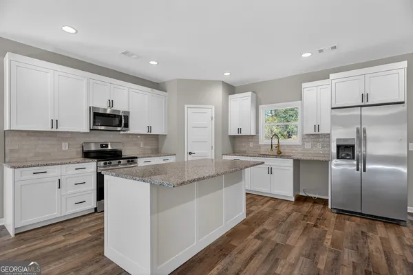 a kitchen with stainless steel appliances granite countertop a stove a sink dishwasher a refrigerator and white cabinets with wooden floor