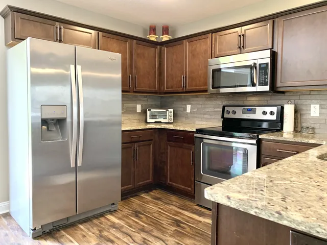 a kitchen with stainless steel appliances granite countertop a refrigerator a stove and a sink with wooden floor