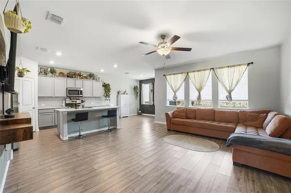 a living room with stainless steel appliances kitchen island granite countertop a couch wooden floor and a large window