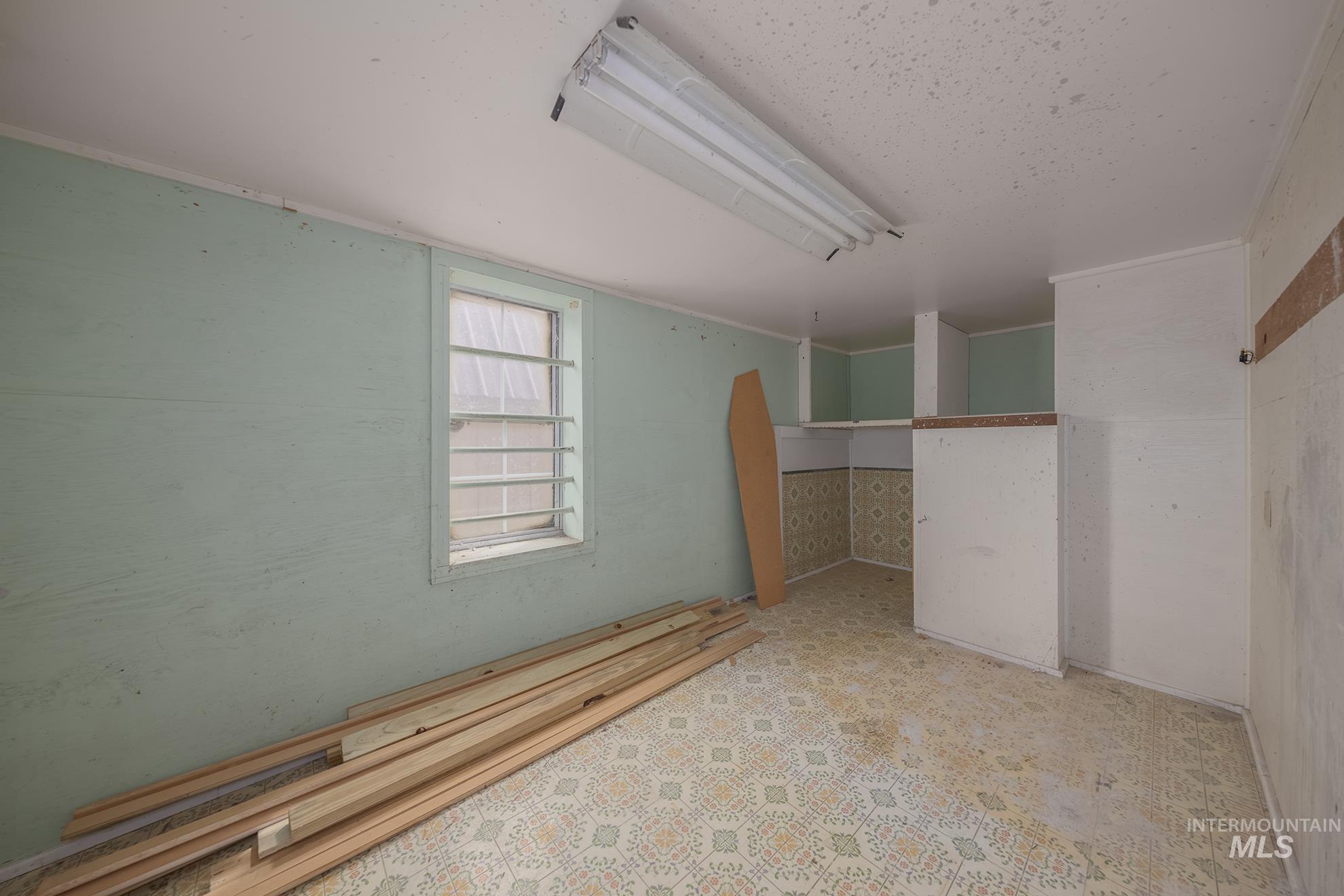 61 Southwest 4th Street Ontario, OR 97914 - Photo 39 of 42 Utility room featuring a window with security bars, built-in shelving, patterned floor covering, and fluorescent overhead lighting
