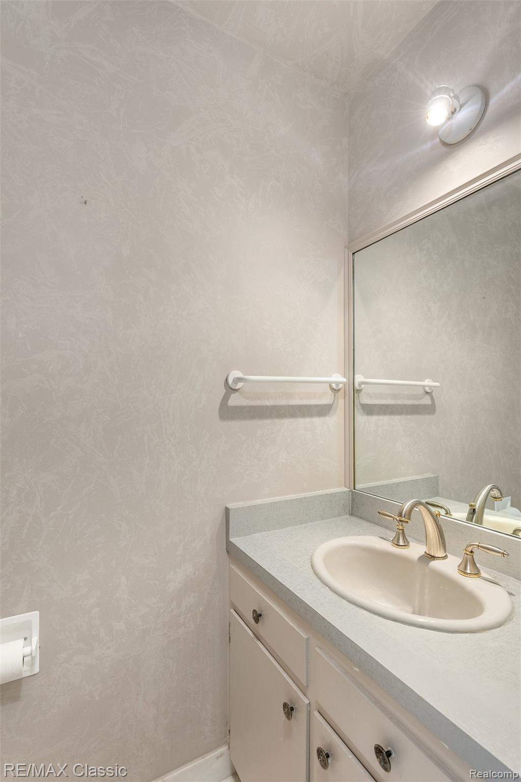 4268 Covered Bridge Road Bloomfield Hills, MI 48302 - Photo 12 of 35 Bathroom featuring a single vanity with a laminate countertop and integrated sink, a wall-mounted mirror, and a brass-finish faucet