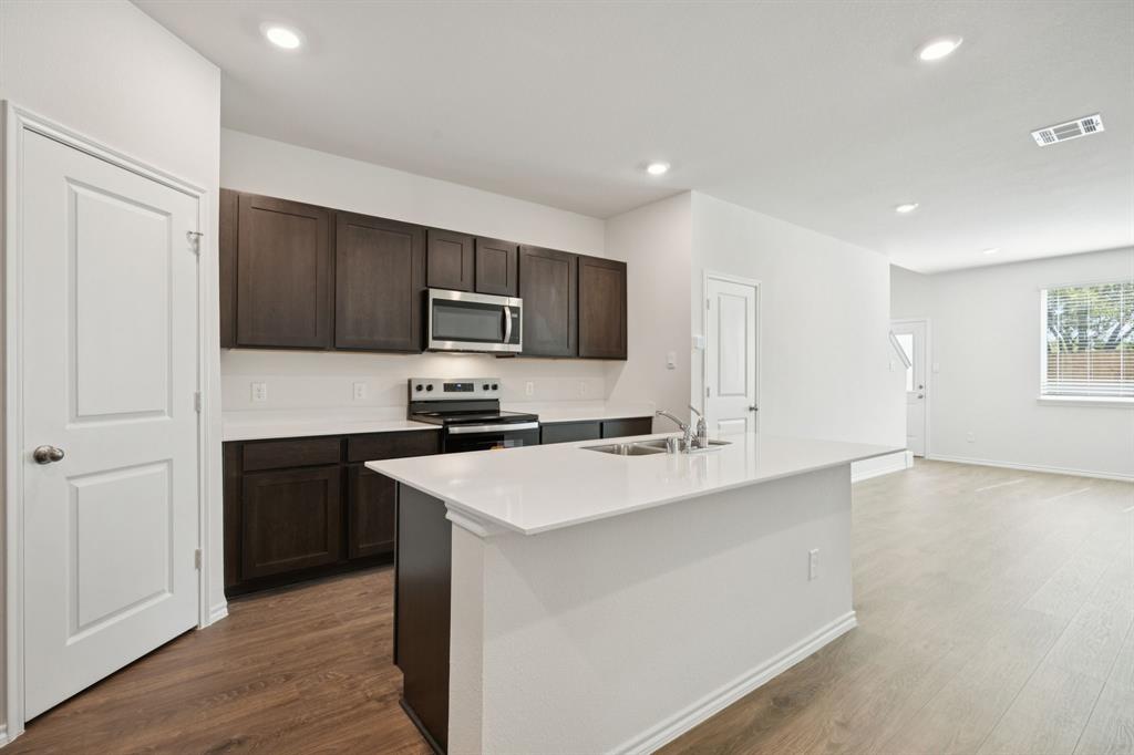 323 Clematis Street Princeton, TX 75407 - Photo 10 of 34 Kitchen with dark brown cabinetry, stainless steel appliances, dark wood finished floors, a kitchen island with sink, and recessed lighting