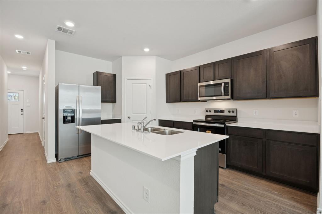 323 Clematis Street Princeton, TX 75407 - Photo 12 of 34 Kitchen featuring appliances with stainless steel finishes, dark brown cabinetry, light wood-style flooring, recessed lighting, and an island with sink