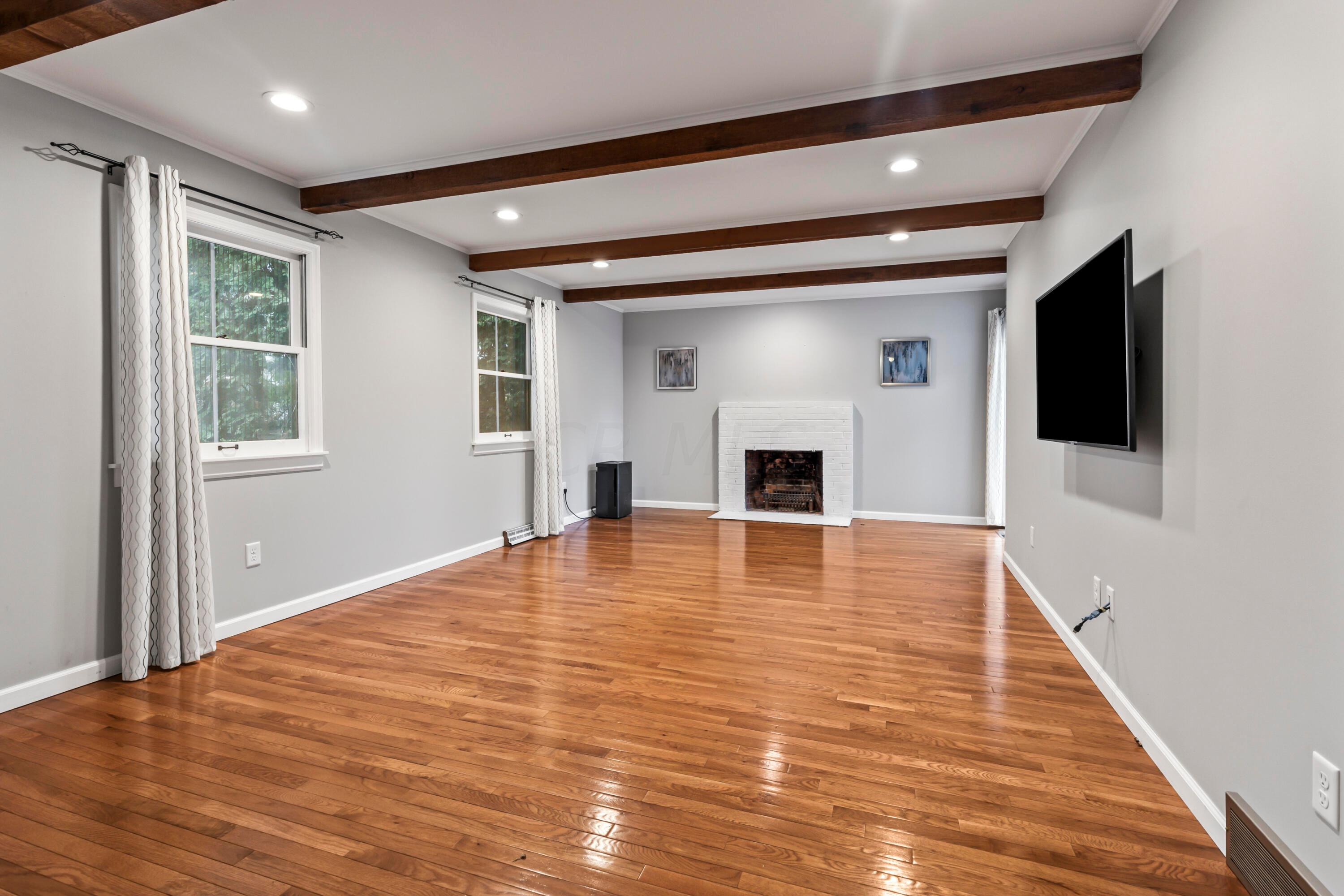 7020 Rieber Street Columbus, OH 43085 - Photo 18 of 40 • New hardwood flooring ~ 2017 • Grey painted walls • Decorative ceiling beams • Can lighting • Wood burning, white painted brick fireplace • Drapes are negotiable • New double sliding doors to patio • TV & mount are negotiable