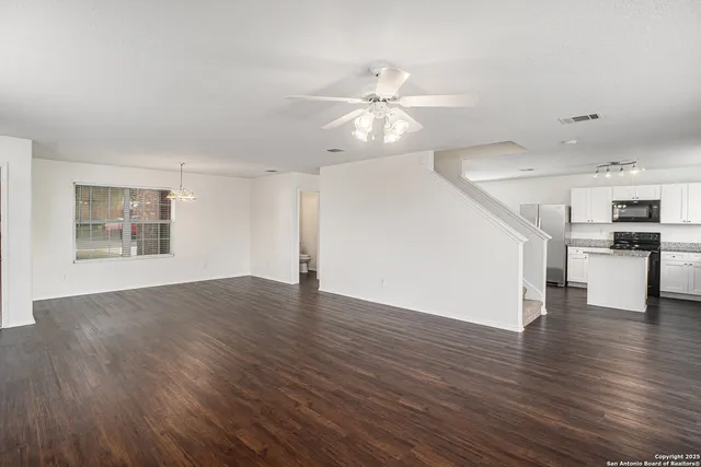 a view of an empty room with wooden floor and a ceiling fan