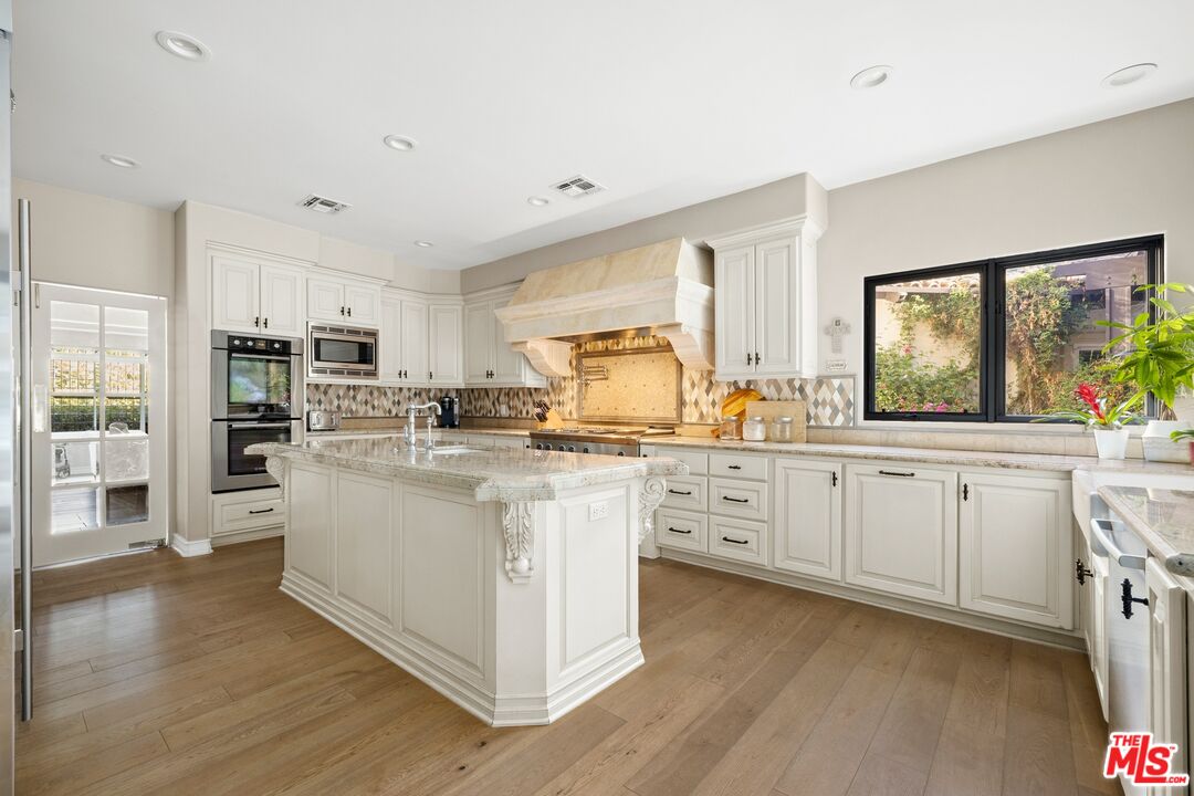 25217 Eldorado Meadow Road Hidden Hills, CA 91302 - Photo 7 of 28 a large white kitchen with granite countertop a stove top oven a sink a dining table and chairs