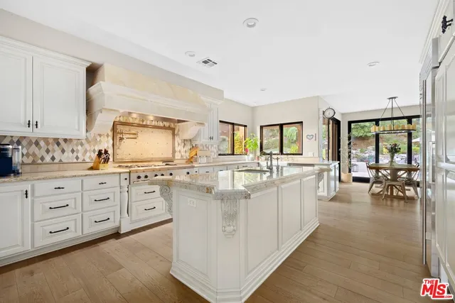 a large white open kitchen with stainless steel appliances kitchen island a large counter space a sink and living room view