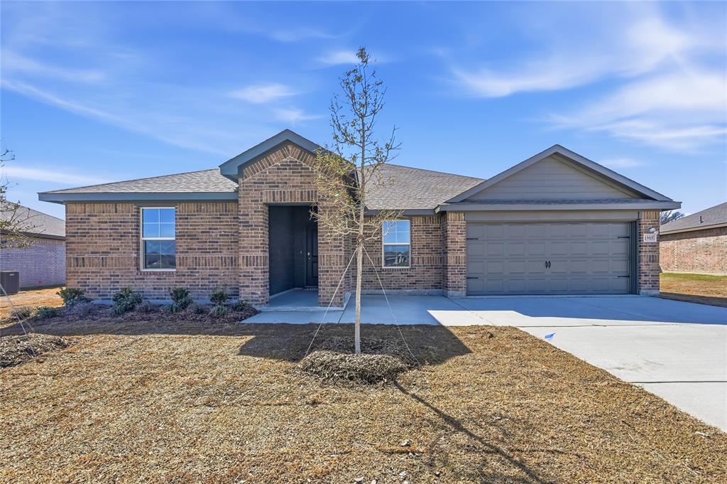 1905 Reveille Way Terrell, TX 75160 - Photo 1 of 6 Brick exterior with a gabled roofline, featuring a two-car garage with a panel door, a concrete driveway, a covered entry, and front landscaping