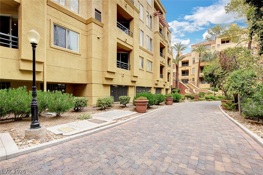 230 East Flamingo Road, Unit 106 Las Vegas, NV 89169 - Photo 28 of 66 A paver block driveway leads to an elegant stucco multi-story building surrounded by mature landscaping.